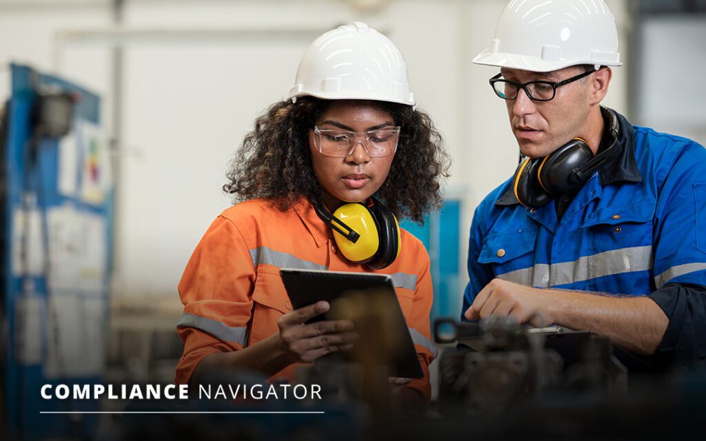 Two workers in a manufacturing facility, wearing hard hats, both looking at a tablet. Text overlays the image, promoting a blog post titled “Compliance Navigator”.
