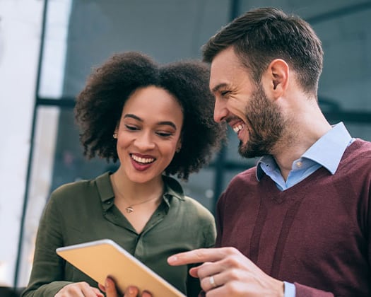 A Black woman is smiling while a man points at a tablet he is holding.