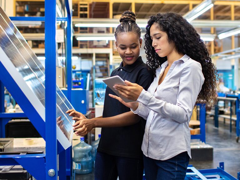 Two people in a factory setting, one using a touchscreen panel while the other reviews workforce analysis software on a tablet.