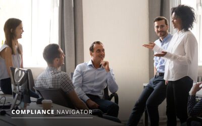 Five people having a discussion in an office setting. One person is standing while the others are seated. Text on image: "Compliance Navigator.