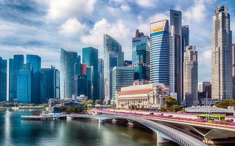 Skyline of a city with modern skyscrapers, a bridge over a body of water, and a clear blue sky.