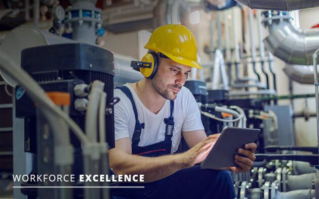 A worker in overalls and a yellow hard hat uses a tablet in an industrial setting, showcasing the benefits of workforce management software. Text reads "Workforce Excellence.