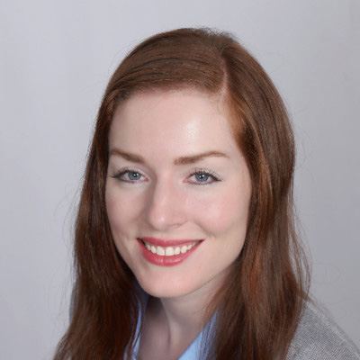 A person with long red hair smiles at the camera against a plain background.