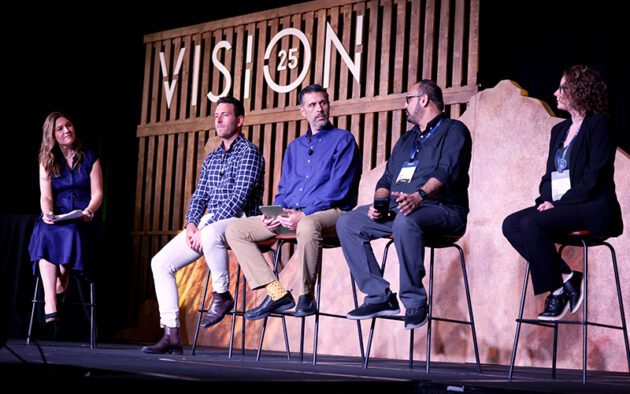 Five people sit on high stools on a stage, engaged in a panel discussion in front of a "VISION 25" sign.