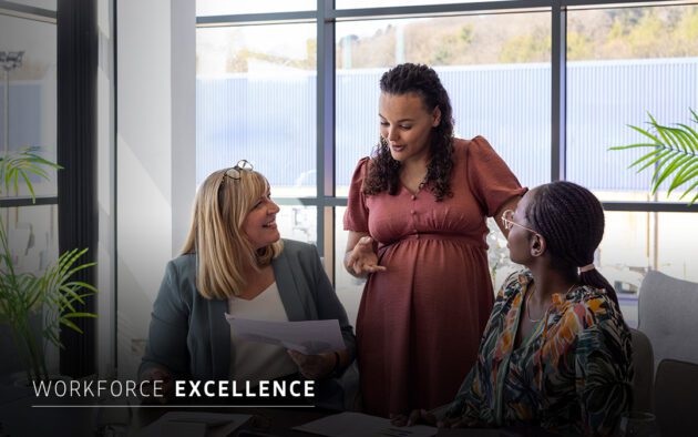 Three women sit and stand around a table in an office, engaged in conversation with documents, with "WORKFORCE EXCELLENCE" text overlayed.