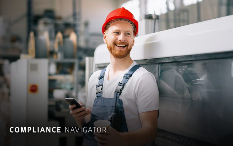 A man in a red hard hat and overalls stands by industrial equipment, holding a smartphone and a cup, with the text "COMPLIANCE NAVIGATOR" on the image, highlighting effective compliance strategies on-site.