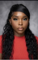 A person with long, wavy black hair wearing a red top poses against a gray background, embodying the diversity of the global workforce while looking directly at the camera with a neutral expression.